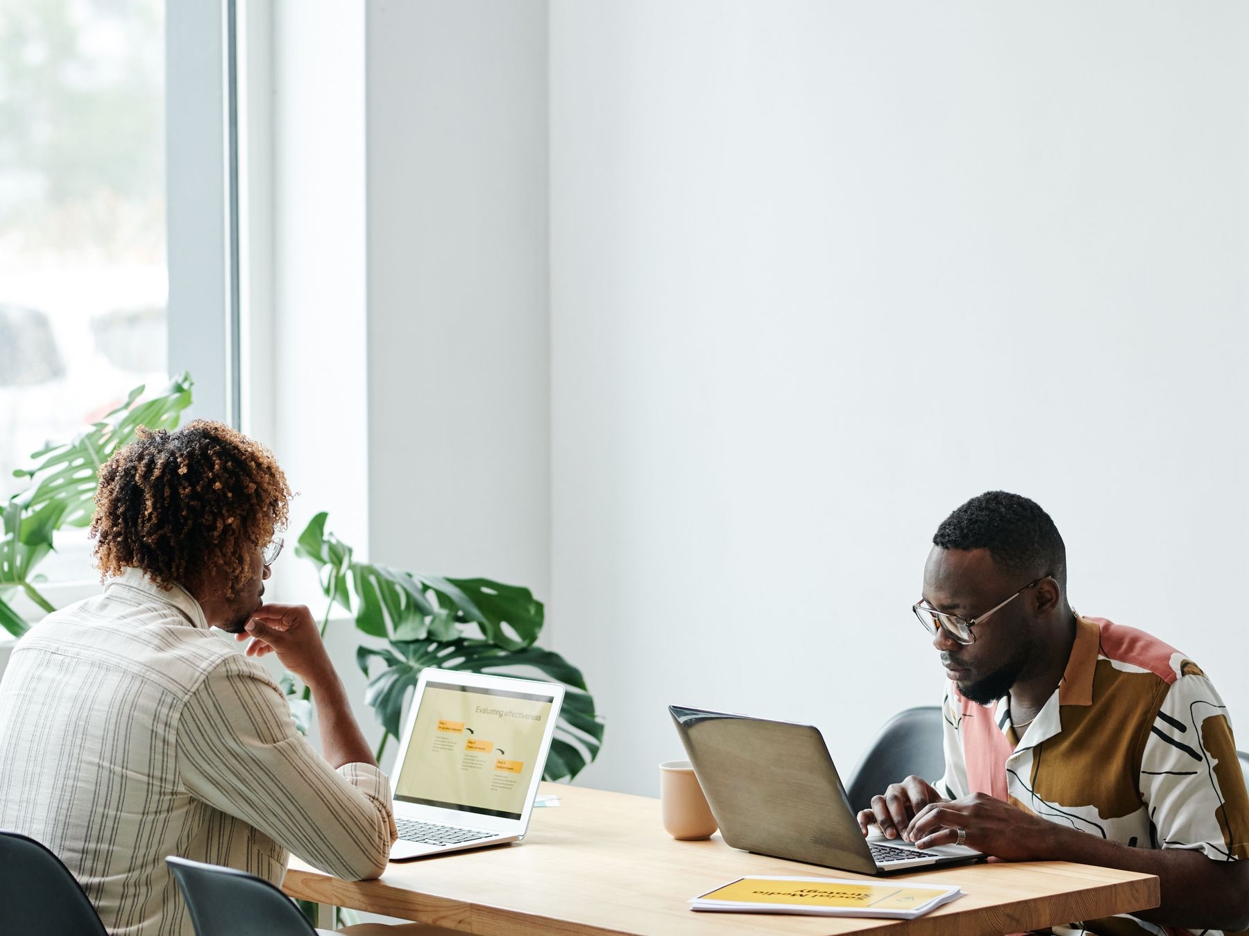Two colleagues working across a table on laptops in a bright office